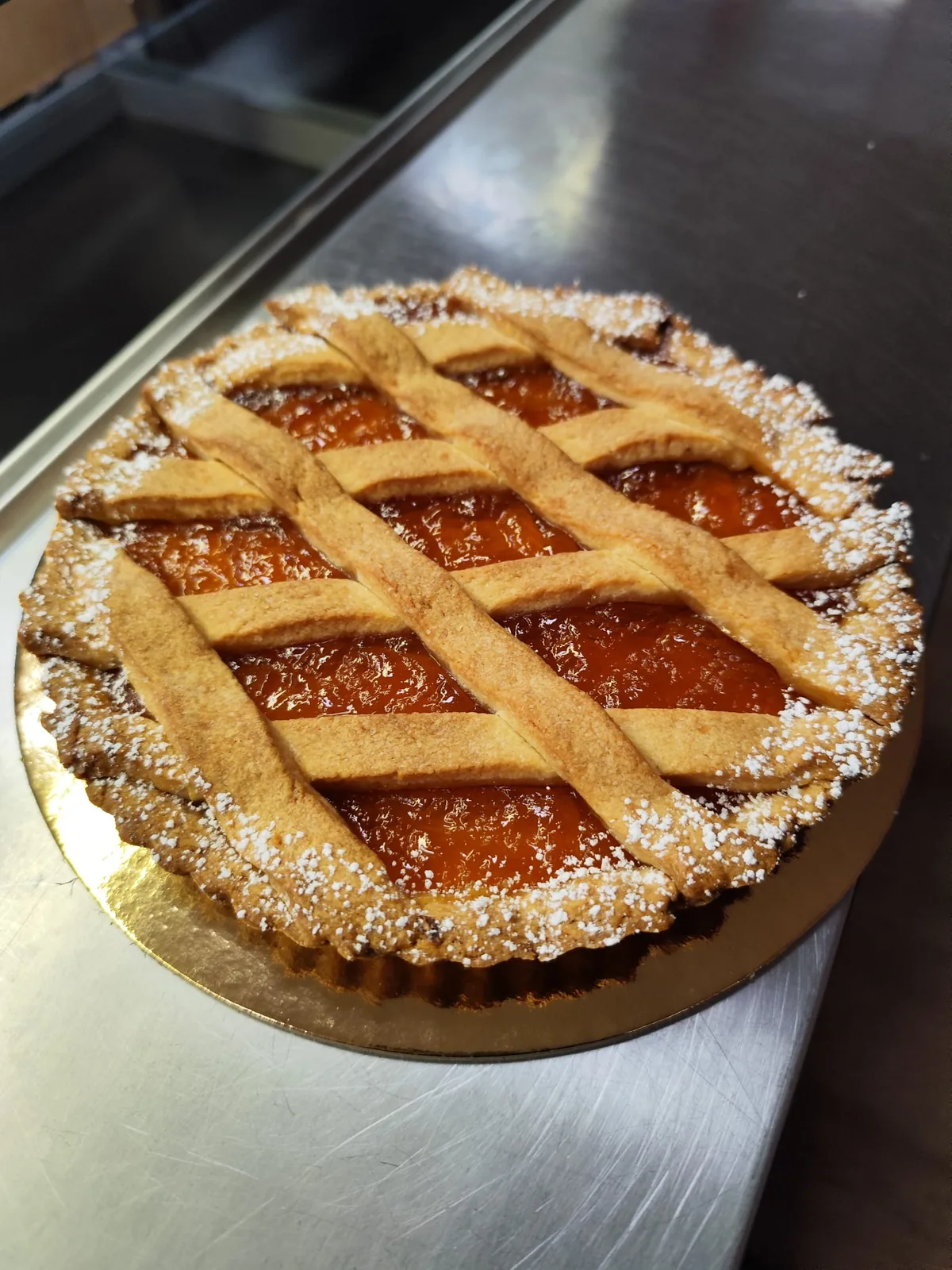 Crostata di albicocche con la griglia di pasta frolla e una spolverata di zucchero a velo.