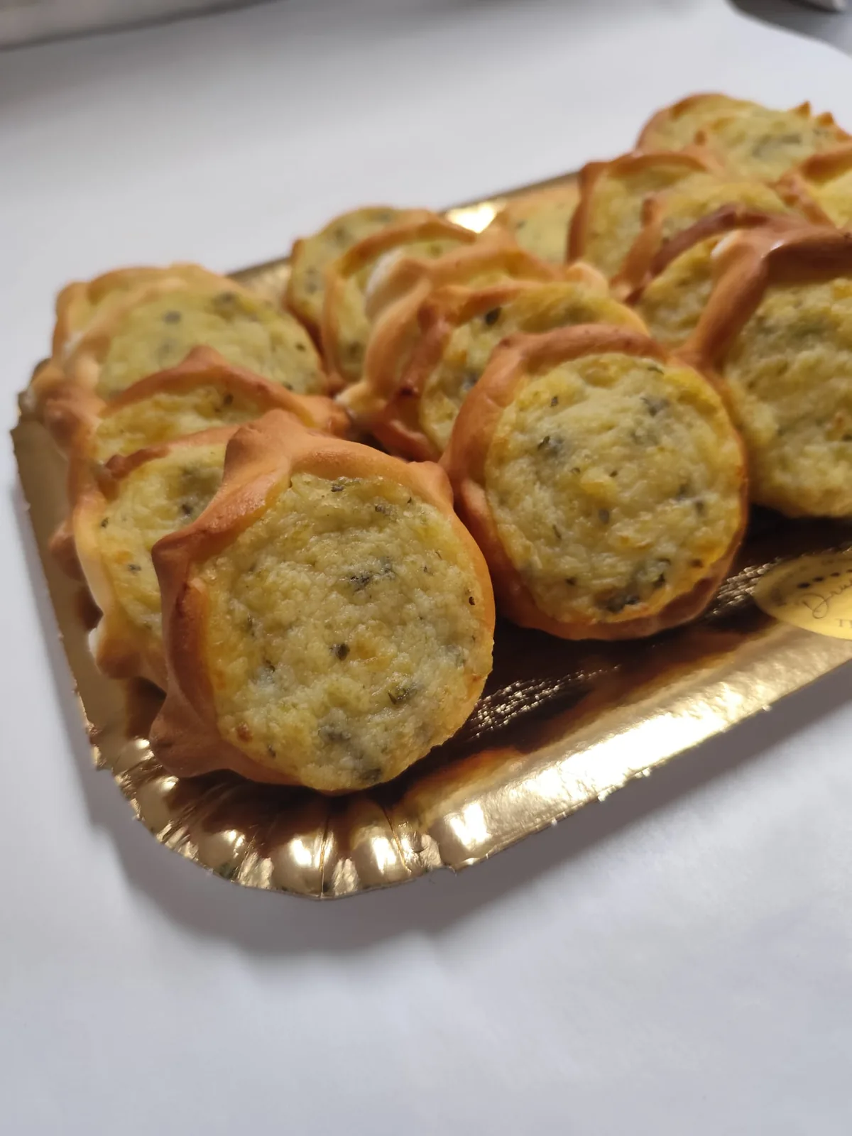 Pardulas salate appena sfornate, con il ripieno di formaggio ed erbe, su un vassoio dorato.